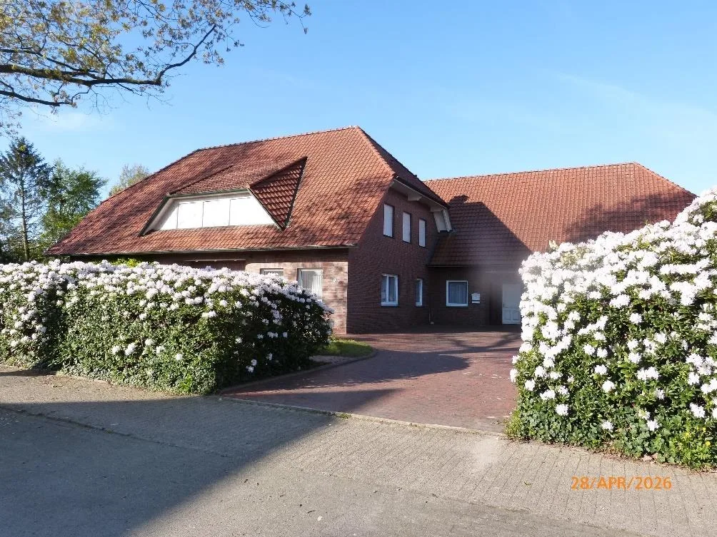 Straßenansicht Wohnhaus mit blühenden Rhododendron-Hecken und Zufahrt