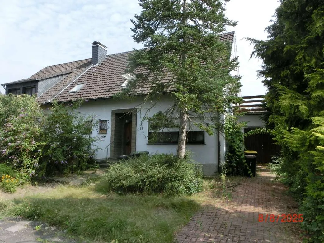 Frontansicht des Wohnhauses mit Satteldach, Vorgarten und Zufahrt, Gebäude gut sichtbar.