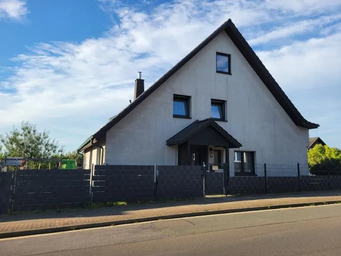 Modern house with white/light facade, black gabled roof, dark fence, street-facing front view