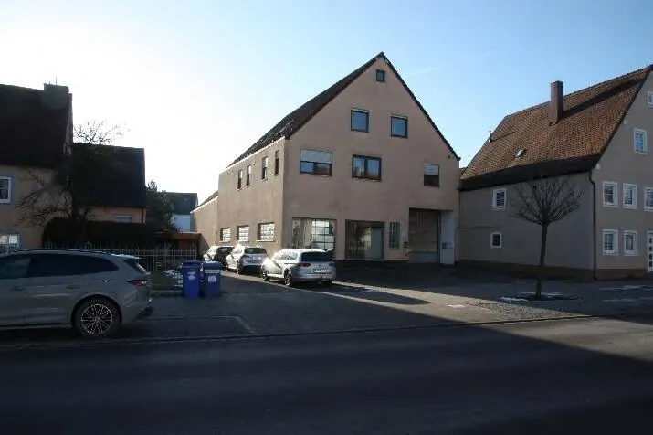 Straßenseitige Außenansicht eines größeren Wohn- und Geschäftsgebäudes mit Satteldach, im Vordergrund parkende Pkw.