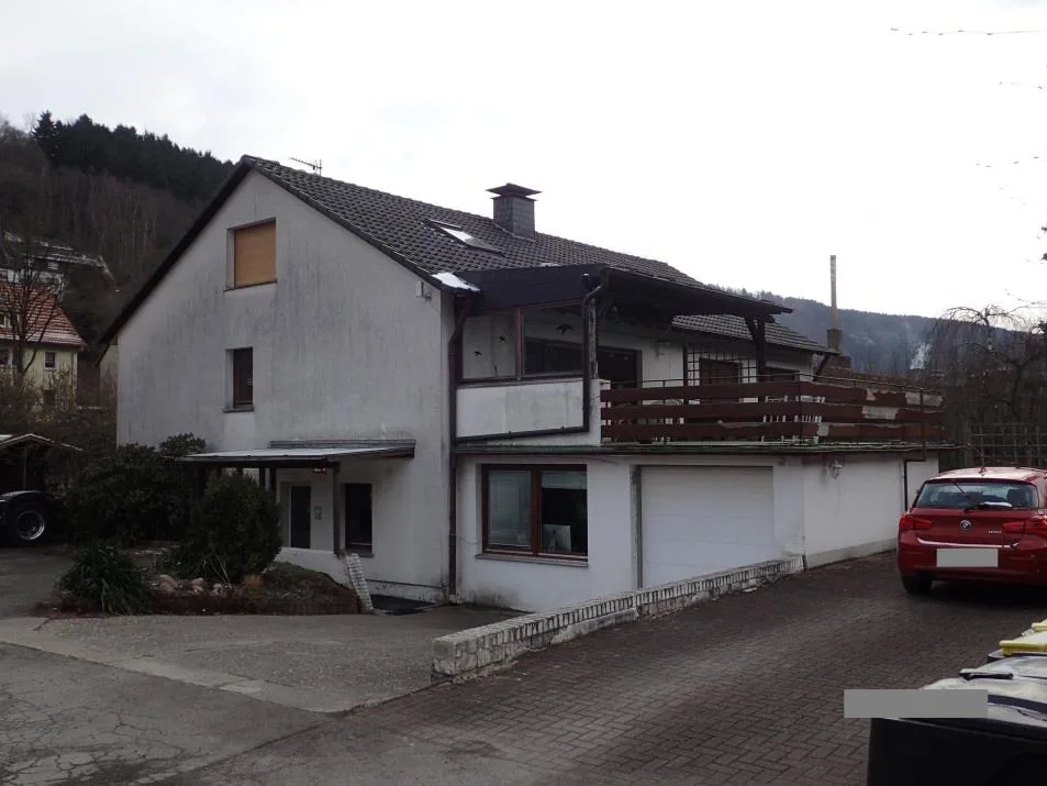 Außenansicht eines Wohnhauses mit Garage, Balkon und gepflasterter Zufahrt, Kfz im Vordergrund.