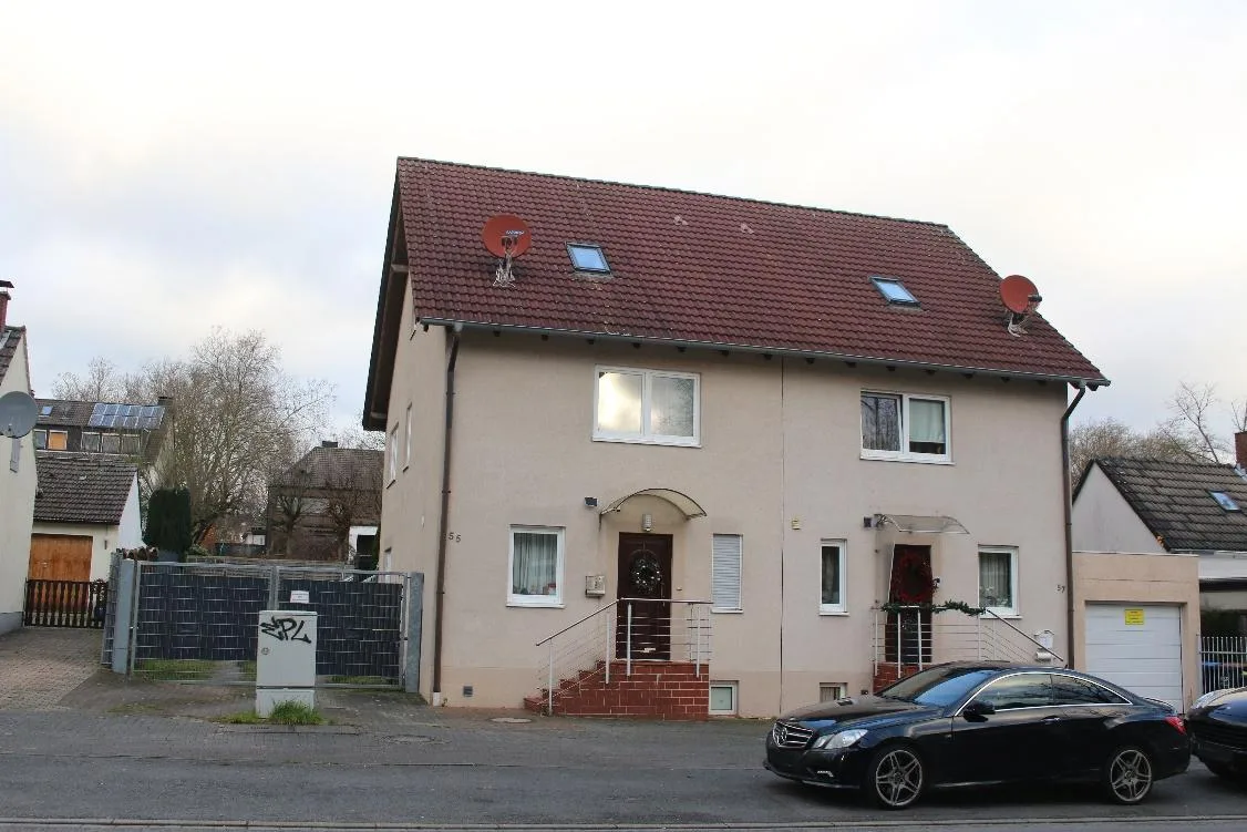 Straßenseitige Hausansicht eines zweigeschossigen Wohnhauses mit Satteldach, Eingangsbereich und Garage im Hintergrund.