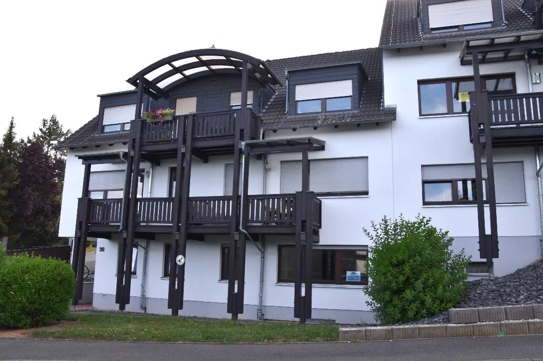 Außenansicht eines Mehrfamilienhauses mit Balkonen, Satteldach und Gartenstreifen davor.