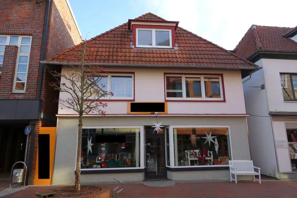 Straßenansicht eines zweigeschossigen Wohn- und Geschäftshauses mit Satteldach, Ladenfenstern und Gehweg.