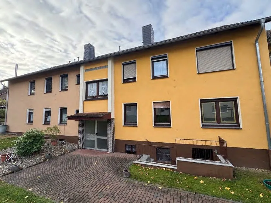 Frontansicht des gelb verputzten Mehrfamilienhauses mit Eingangsbereich und Vorgarten.
