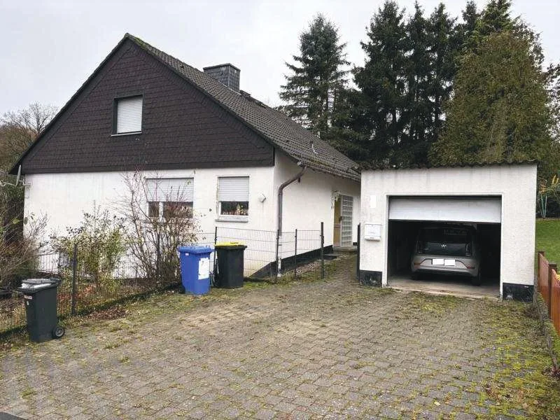 Wohnhaus mit dunklem Giebel und angebauter Garage, von vorne, Zufahrt mit Pflasterstein.